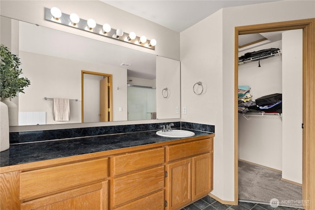 bathroom featuring a walk in closet, baseboards, visible vents, and vanity