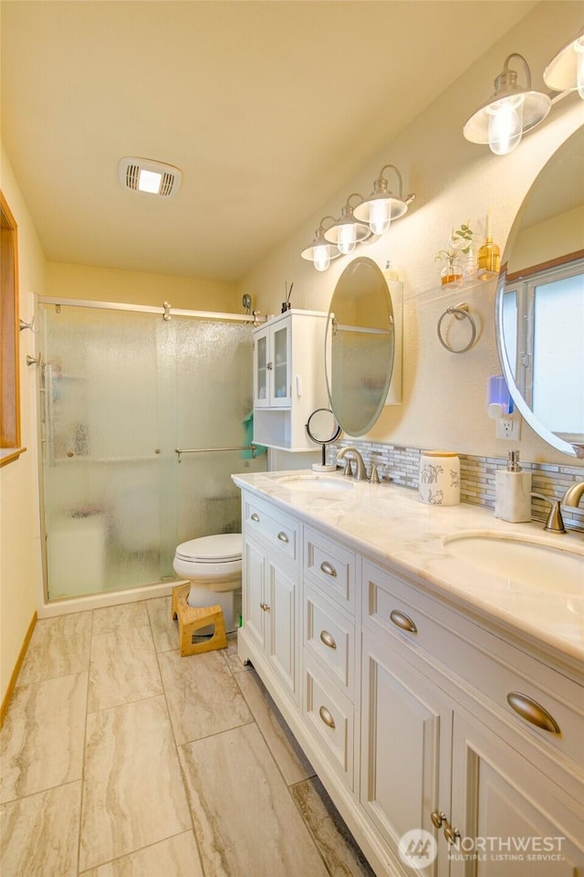 bathroom with visible vents, toilet, a sink, a shower with door, and double vanity