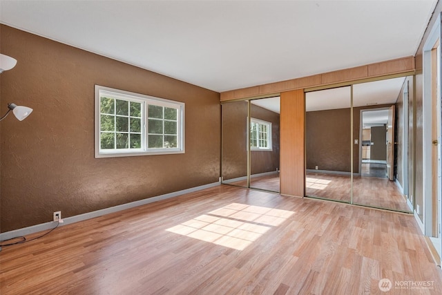 unfurnished bedroom with a textured wall, wood finished floors, baseboards, and two closets