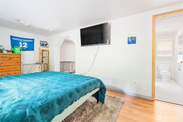 bedroom featuring wood finished floors, baseboards, and connected bathroom