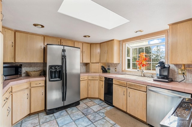 kitchen with light brown cabinetry, stainless steel appliances, tile counters, and a sink