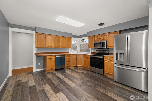 kitchen with a sink, stainless steel appliances, light countertops, baseboards, and dark wood-style flooring