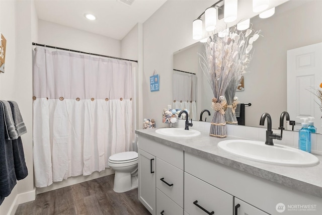 bathroom with a sink, toilet, wood finished floors, and double vanity