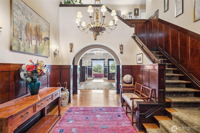 foyer entrance featuring wood finished floors, a wainscoted wall, arched walkways, stairs, and a notable chandelier