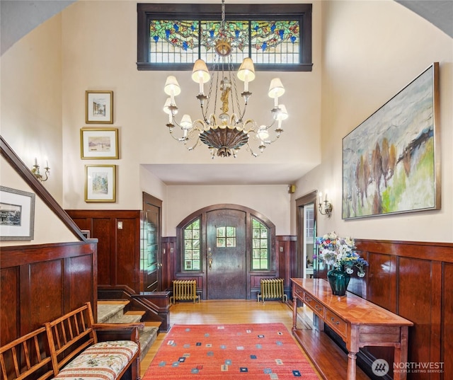 foyer featuring a wainscoted wall, radiator heating unit, wood finished floors, arched walkways, and a notable chandelier