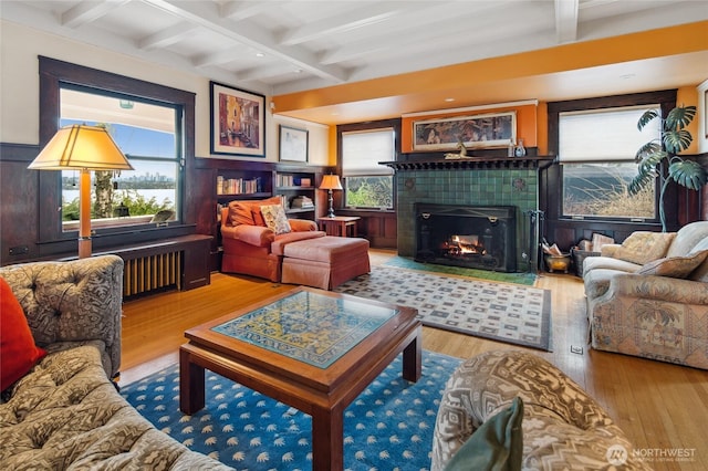 living area with beamed ceiling, wood finished floors, a wainscoted wall, and a tile fireplace