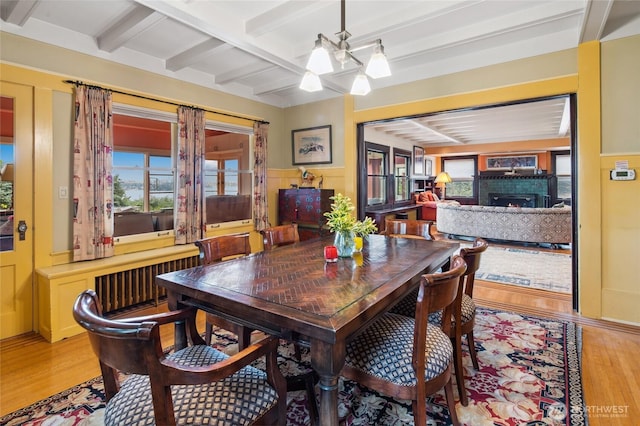 dining space with light wood-type flooring, radiator heating unit, beam ceiling, a tile fireplace, and a decorative wall