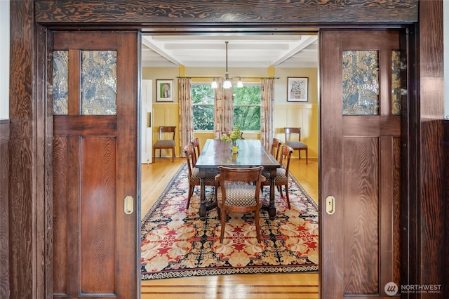 dining area with a notable chandelier, a decorative wall, wainscoting, and wood finished floors