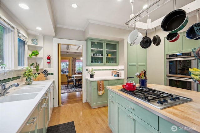 kitchen featuring green cabinetry, a sink, ornamental molding, stainless steel appliances, and light wood-style floors