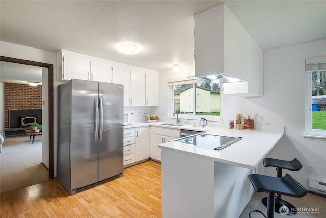 kitchen featuring light countertops, a peninsula, freestanding refrigerator, black electric cooktop, and a sink