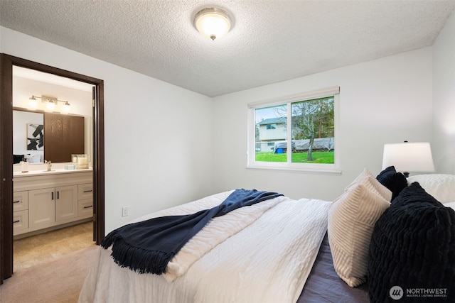 bedroom with a sink, ensuite bath, light colored carpet, and a textured ceiling