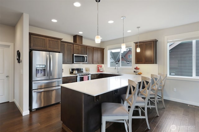 kitchen featuring a peninsula, stainless steel appliances, light countertops, dark wood-type flooring, and backsplash