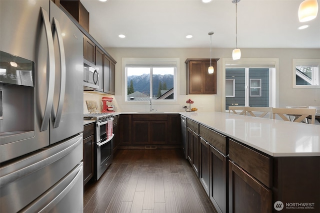 kitchen with dark wood-type flooring, a sink, stainless steel appliances, a peninsula, and light countertops