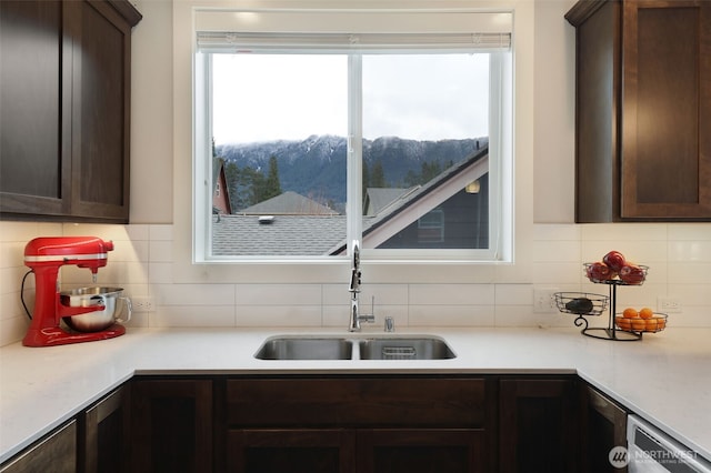 kitchen featuring a sink, a mountain view, dark brown cabinetry, light countertops, and dishwashing machine