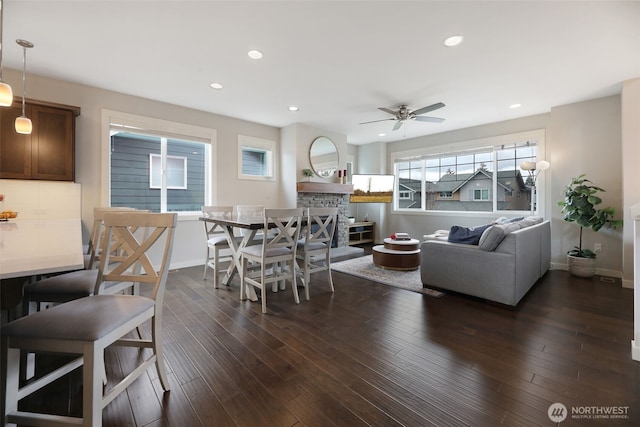 dining room with a ceiling fan, baseboards, recessed lighting, a stone fireplace, and dark wood-type flooring