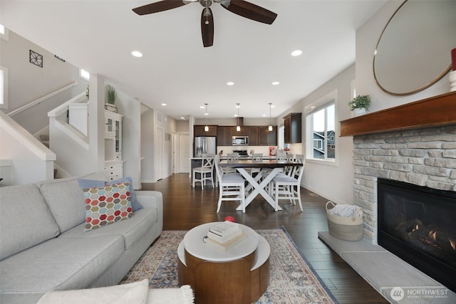 living room with dark wood-type flooring, a glass covered fireplace, recessed lighting, baseboards, and stairs