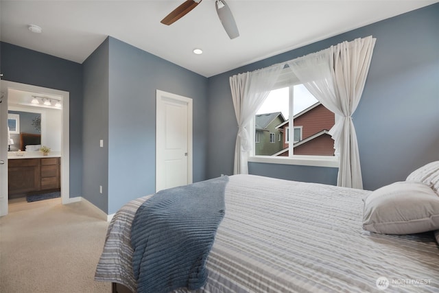 bedroom featuring ceiling fan, baseboards, light colored carpet, and ensuite bath