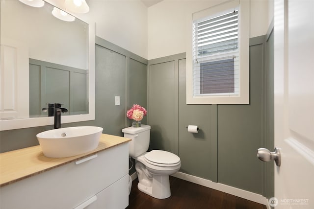 bathroom featuring vanity, wood finished floors, a wainscoted wall, a decorative wall, and toilet