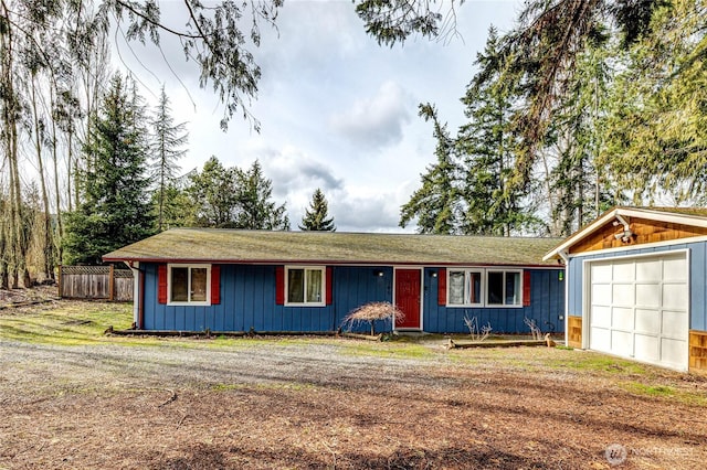 ranch-style house with an attached garage, board and batten siding, fence, an outdoor structure, and driveway