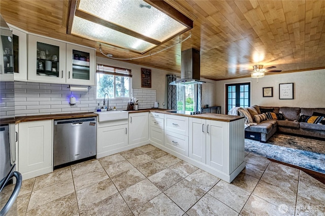 kitchen featuring a peninsula, stainless steel dishwasher, island range hood, wood counters, and a sink