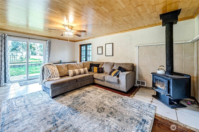 tiled living room with plenty of natural light, wooden ceiling, a wood stove, and ornamental molding