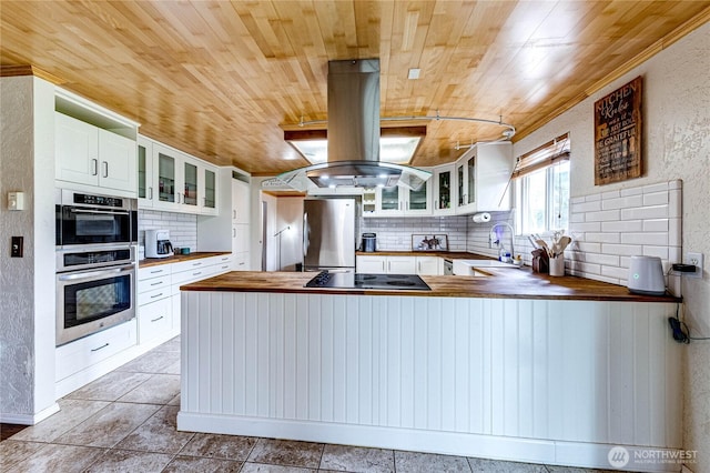 kitchen with butcher block countertops, stainless steel appliances, island range hood, decorative backsplash, and wood ceiling