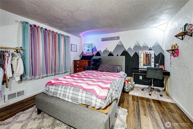 bedroom with visible vents, baseboards, wood finished floors, a textured wall, and a textured ceiling