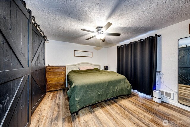 bedroom featuring visible vents, a textured ceiling, a barn door, light wood-style floors, and ceiling fan