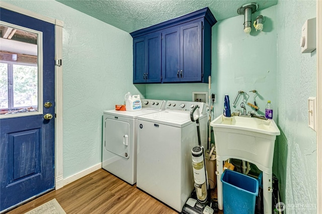 laundry area featuring a textured wall, cabinet space, wood finished floors, and washer and clothes dryer