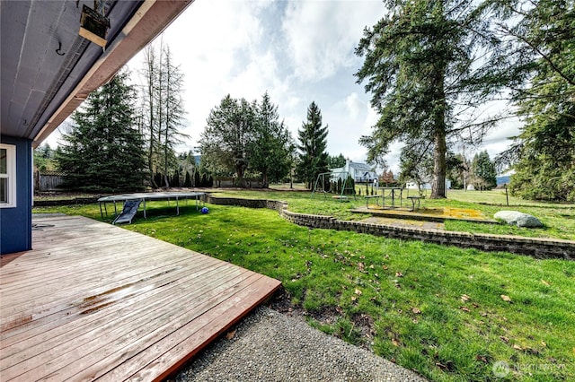 view of yard featuring a wooden deck, a trampoline, and a playground