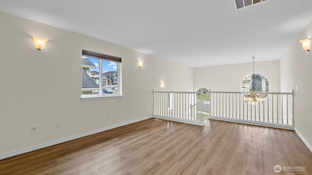 empty room featuring an inviting chandelier, baseboards, and wood finished floors