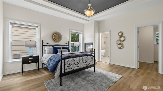 bedroom featuring light wood finished floors, a raised ceiling, and baseboards