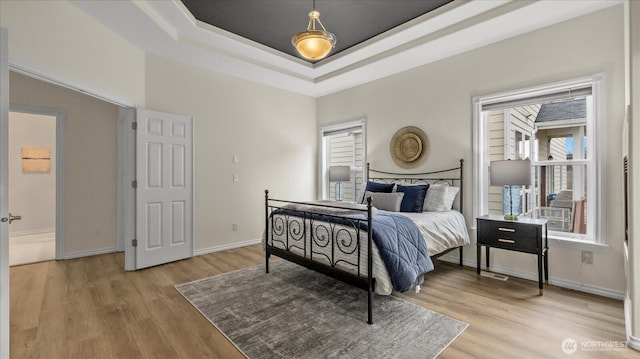 bedroom featuring baseboards, a raised ceiling, and light wood-style floors