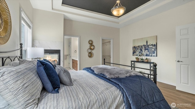 bedroom with ensuite bath, wood finished floors, a high end fireplace, a raised ceiling, and a spacious closet