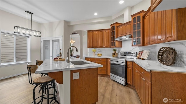 kitchen featuring a kitchen bar, under cabinet range hood, a sink, stainless steel range with electric cooktop, and brown cabinetry