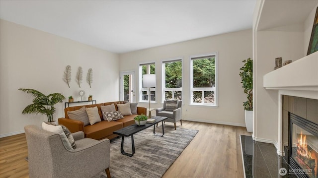 living area featuring a tile fireplace, baseboards, and wood finished floors