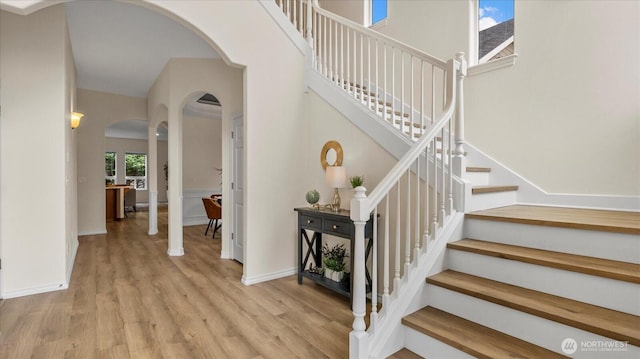 stairs with baseboards, arched walkways, wood finished floors, and a towering ceiling