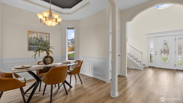 dining area featuring light wood finished floors, a chandelier, stairway, a tray ceiling, and arched walkways