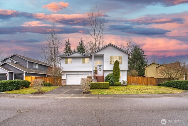 view of front facade featuring an attached garage, a lawn, driveway, and fence