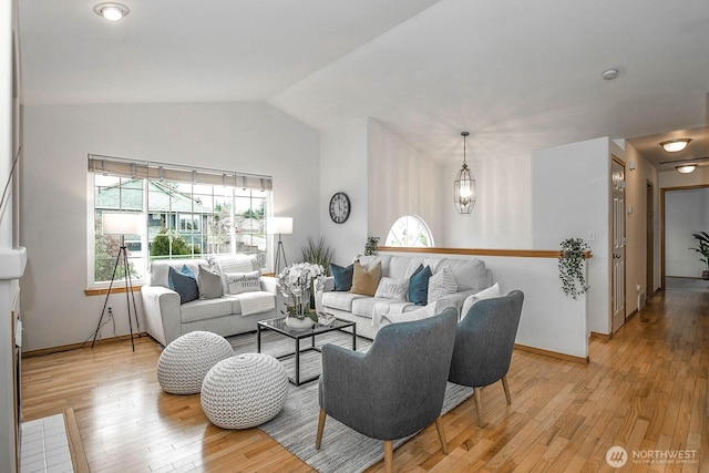 living room with baseboards, lofted ceiling, a notable chandelier, and light wood finished floors