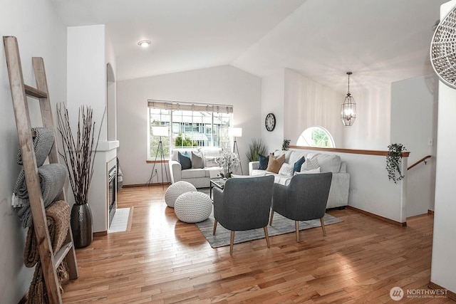 living area with light wood-type flooring, an inviting chandelier, a healthy amount of sunlight, and vaulted ceiling