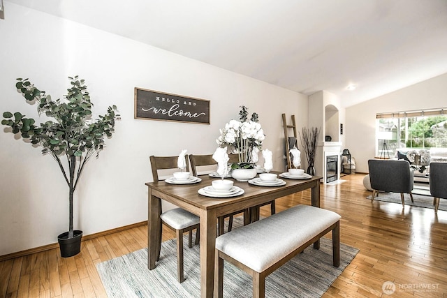 dining room featuring a fireplace with flush hearth, lofted ceiling, beverage cooler, light wood-style flooring, and baseboards