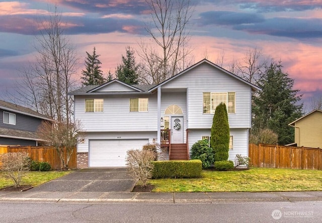 raised ranch with fence, an attached garage, driveway, and a front yard
