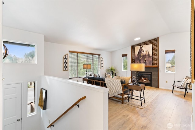 living area featuring vaulted ceiling, light wood-style flooring, and a fireplace