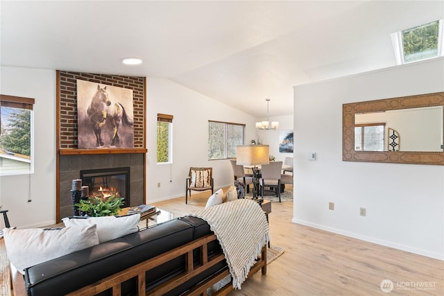 living room featuring vaulted ceiling, a fireplace, light wood finished floors, and a chandelier