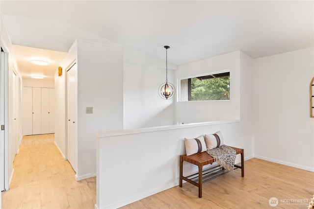 living area with light wood-type flooring, baseboards, a notable chandelier, and lofted ceiling