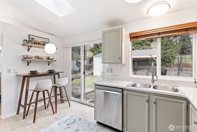 kitchen with a skylight, a sink, gray cabinetry, light countertops, and dishwasher