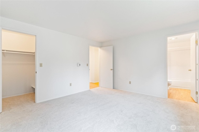 unfurnished bedroom with a walk in closet, carpet, a closet, and connected bathroom