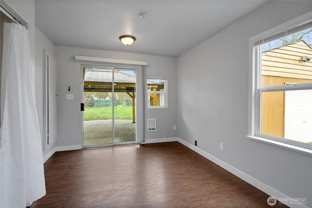 empty room with dark wood finished floors, heating unit, and baseboards