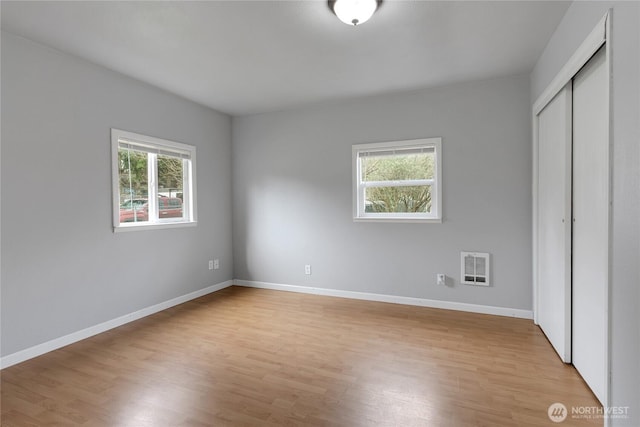 unfurnished bedroom featuring light wood-type flooring, multiple windows, baseboards, and a closet